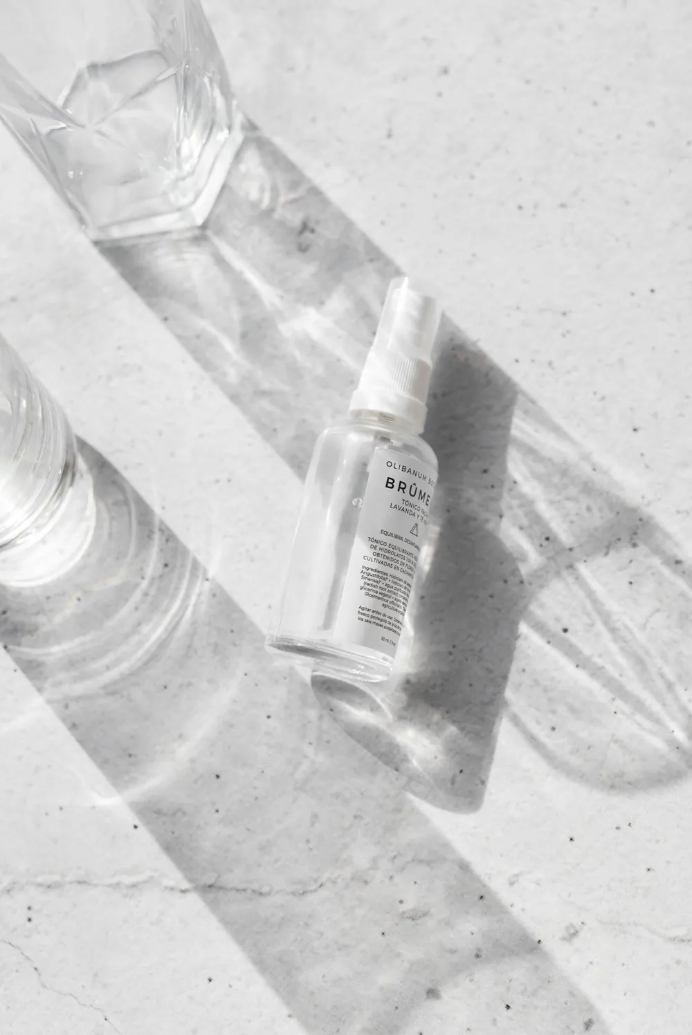 Frasco transparente de cuidado personal sobre superficie blanca con sombras